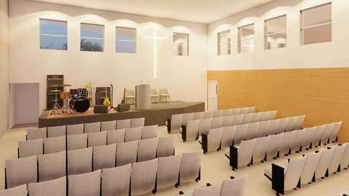 Interior do salão de culto com cadeiras, palco, instrumentos e cruz iluminada